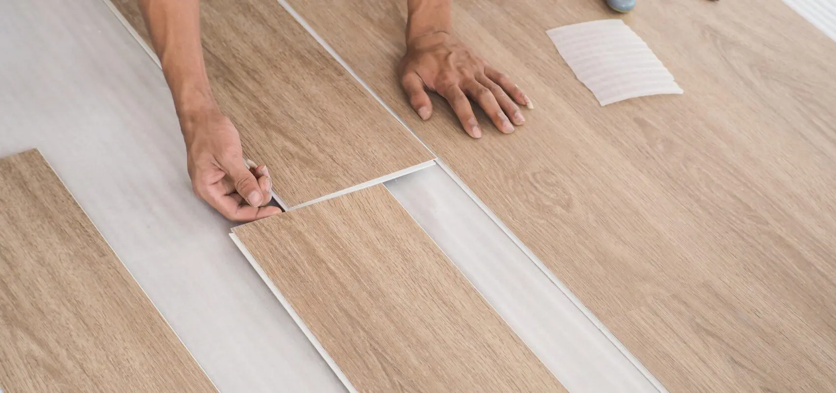 Person installing vinyl plank flooring on a wooden subfloor.