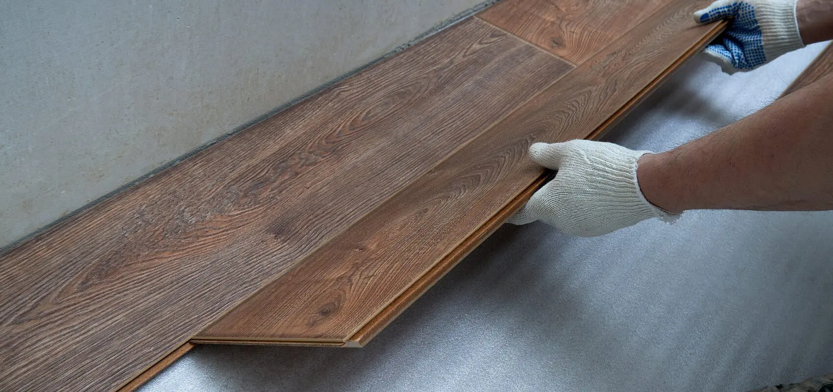 A gloved hand holding a wooden plank with beveled edges.