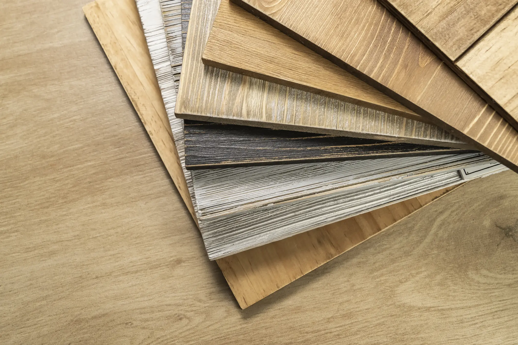 A fan of wood laminate flooring samples in various colors and textures.