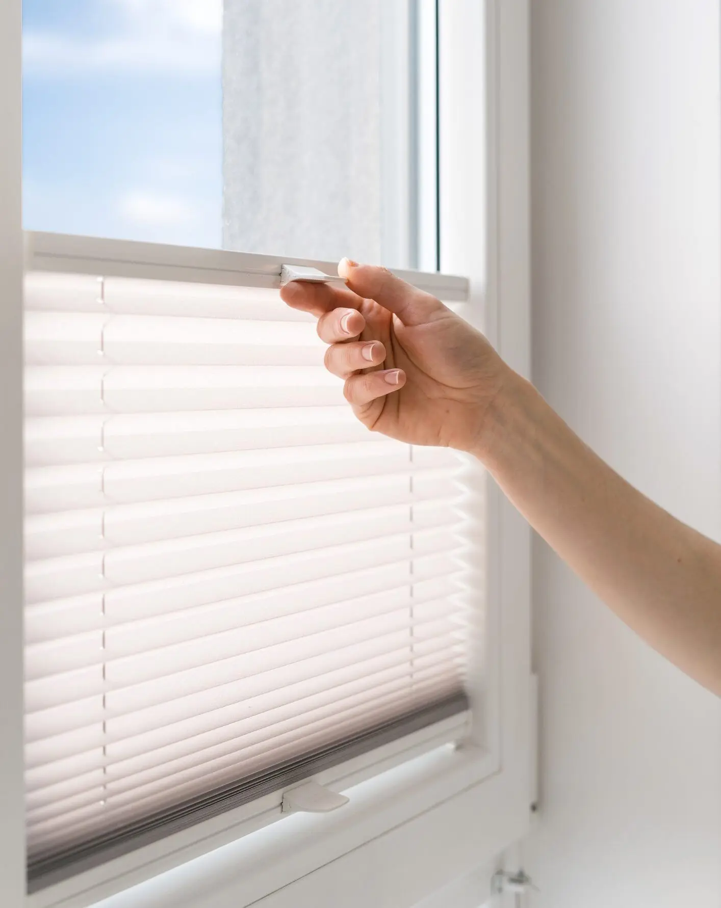 Hand adjusting white window blinds.