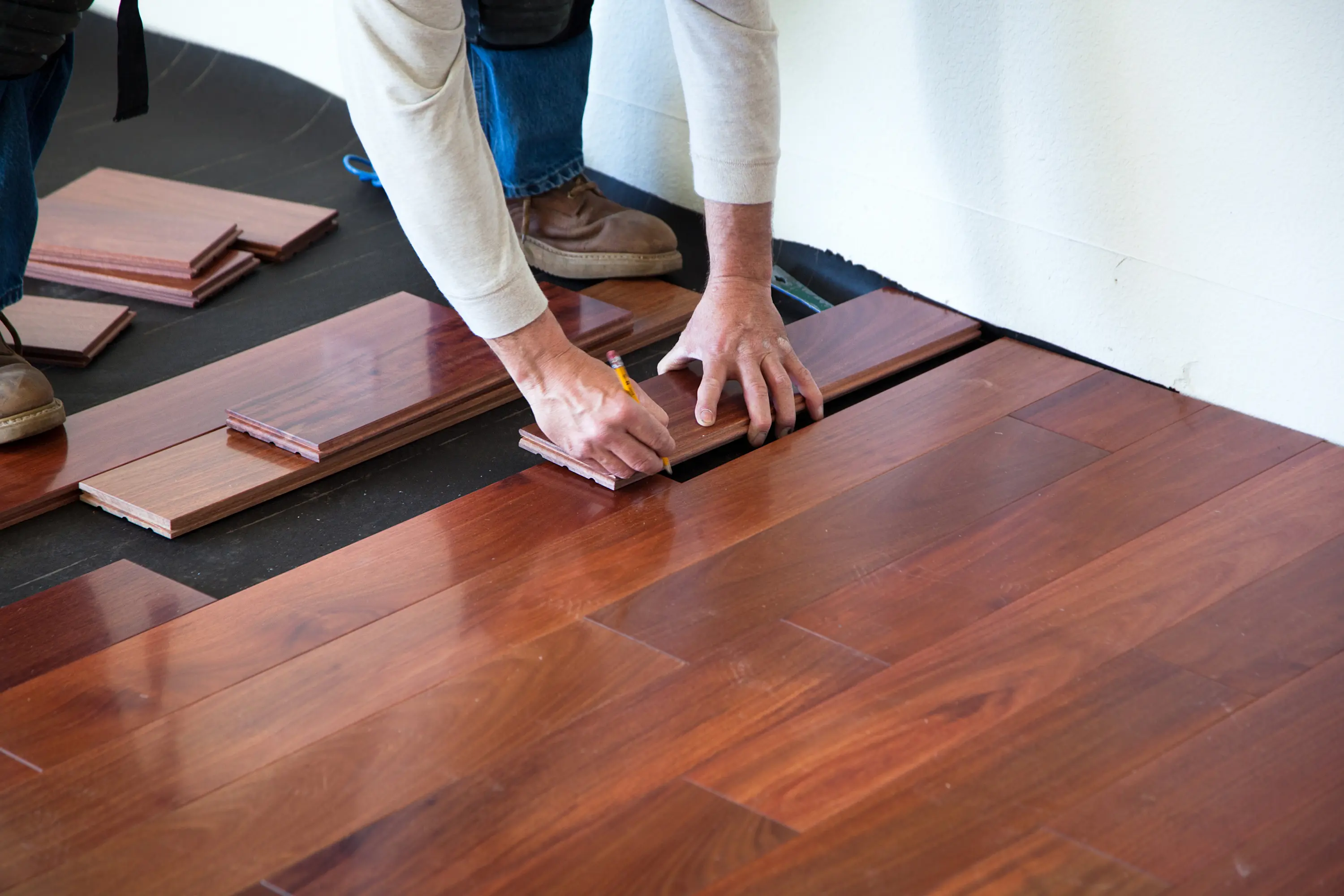 Person installing wooden floor panels by hand indoors.