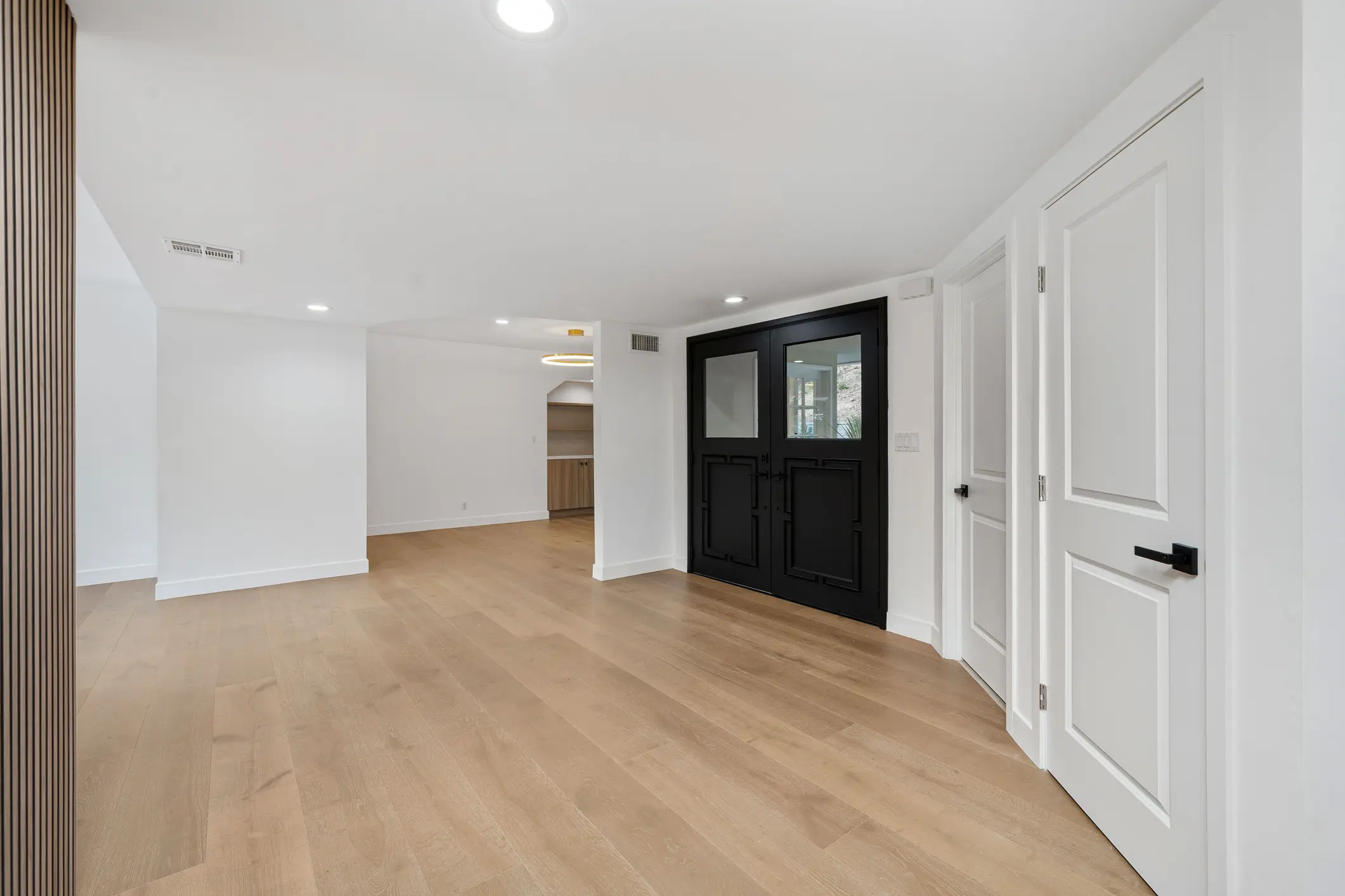 Spacious modern room with light wood flooring and black double doors.
