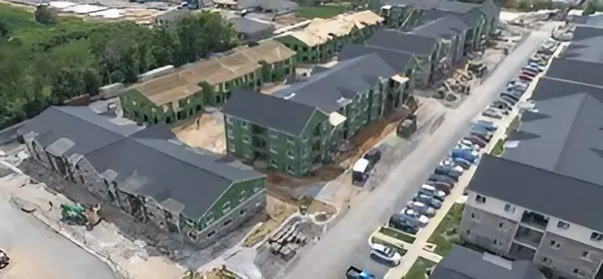 Aerial view of a residential complex with green buildings and parked cars.