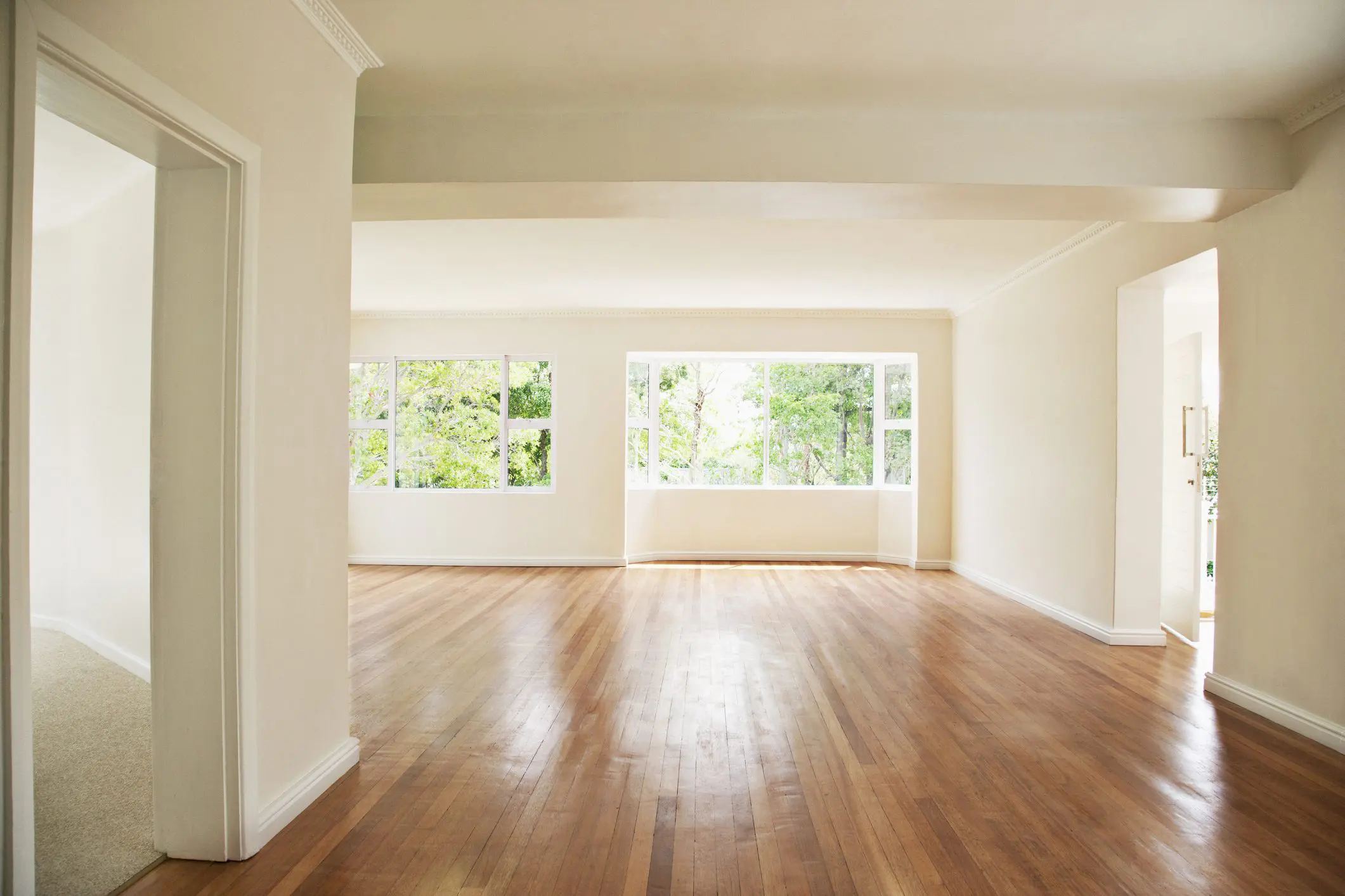 Bright empty room with wooden floors and large windows.