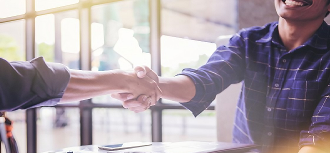 Two people shaking hands in a bright office setting.