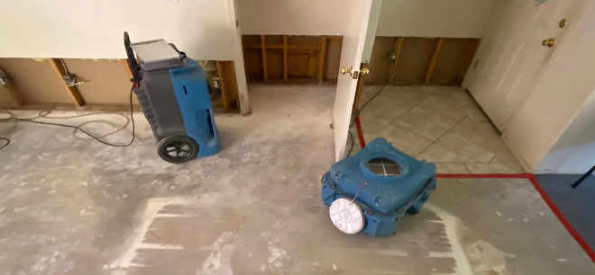 Dehumidifiers drying a flooded room with water damage on walls.